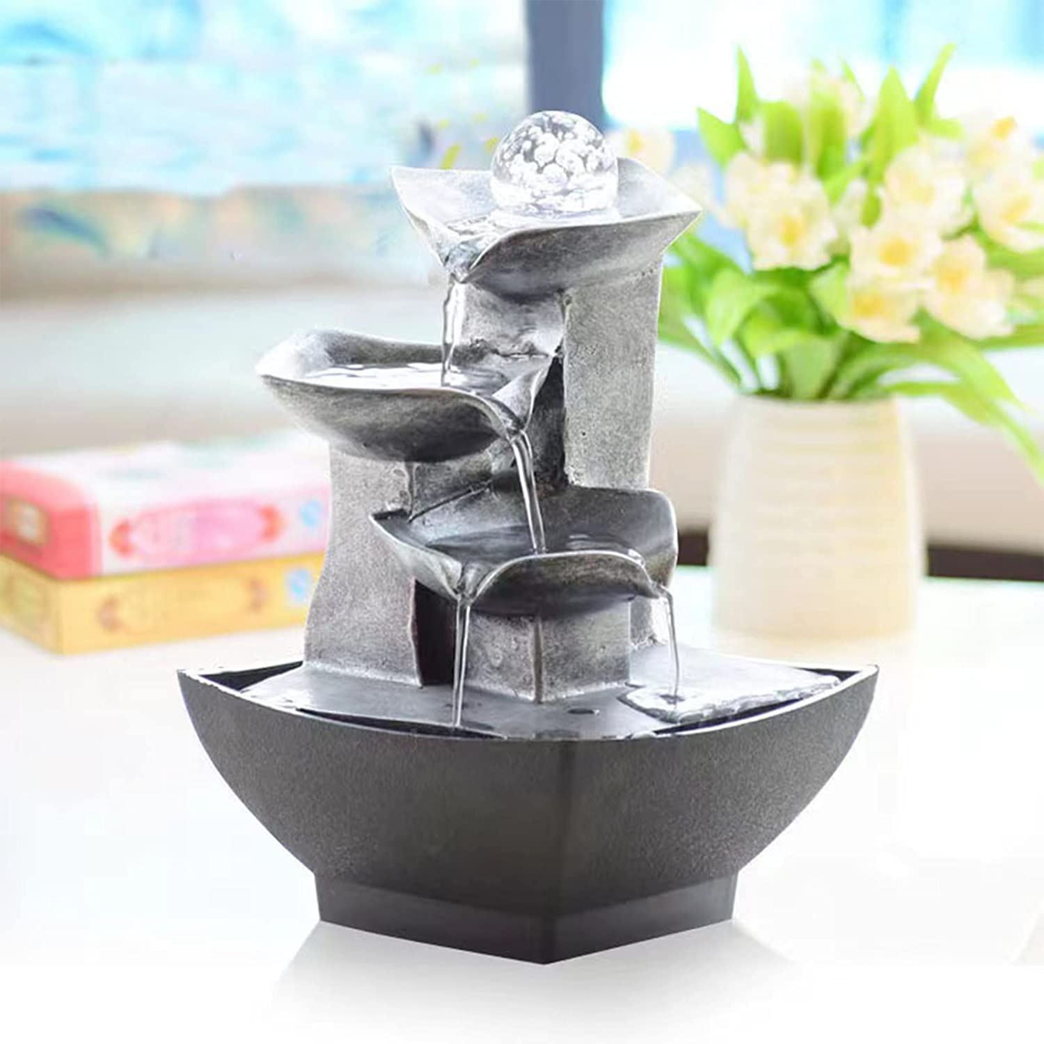 A tabletop water fountain which has 3-tiers. Water is flowing down all 3 tiers into the base of the fountain.