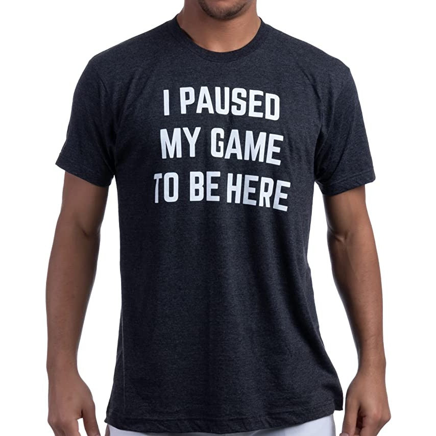 A man is wearing a black t-shirt which has printed white text that says, 'I paused my game to be here.'