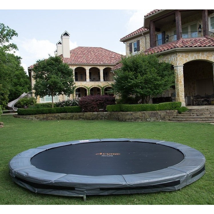 Large circular trampoline installed flush with a landscaped backyard lawn