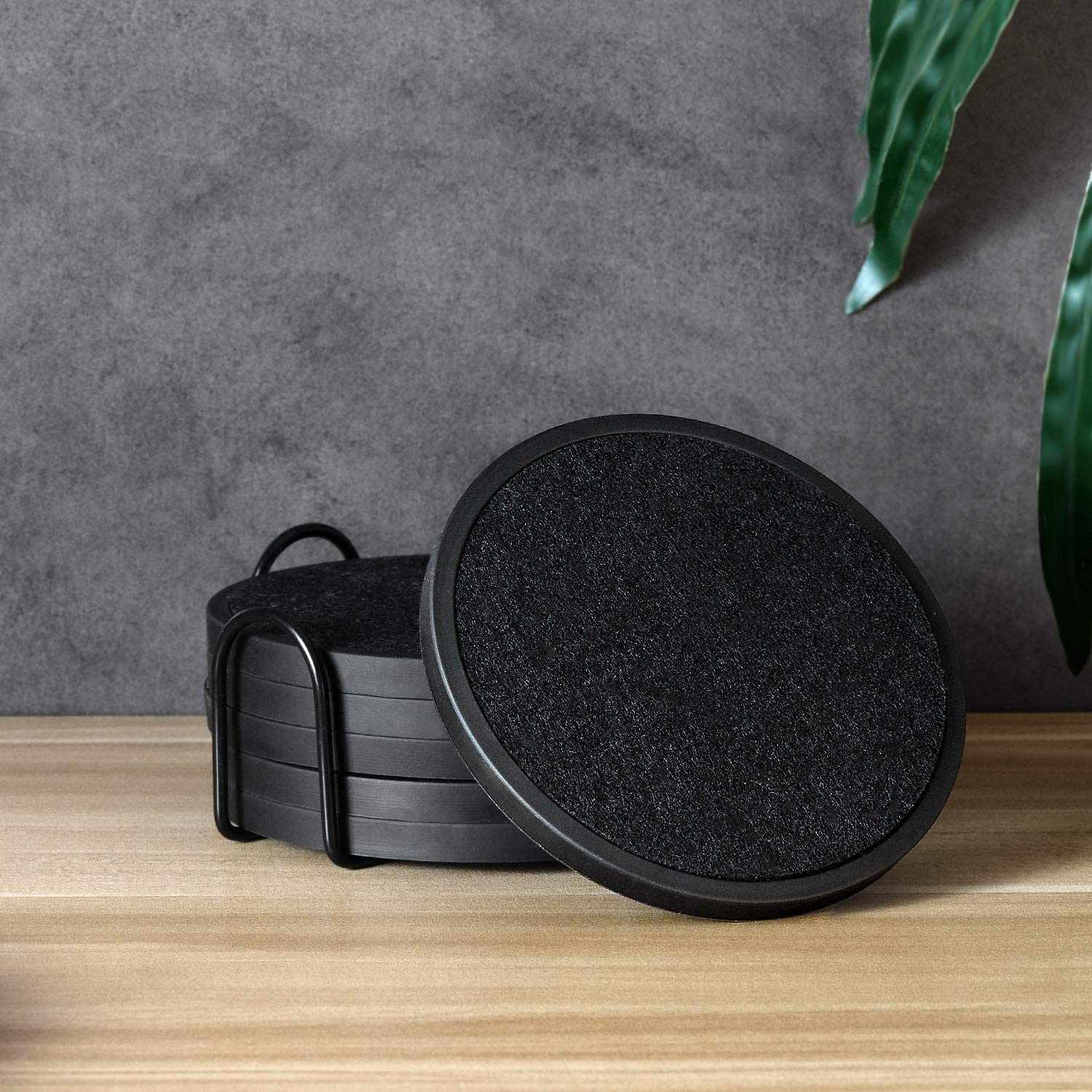 A set of 6 absorbent black coasters in a black metal holder. The set of coasters are on a wooden table.
