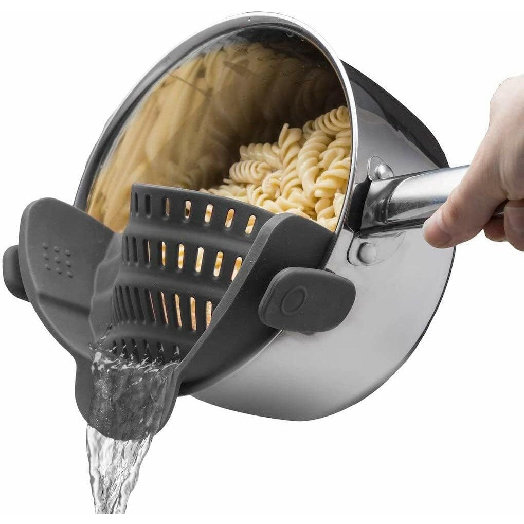 A gray silicone pot strainer is attached to a saucepan draining water out of cooked pasta.