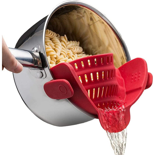 A red colored strainer is attached to a pot to help drain water out of pasta.