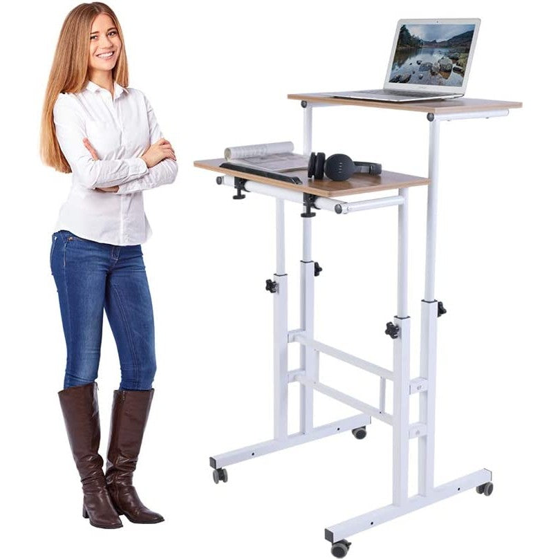 A woman is smiling and standing in front of an adjustable standing desk. There is a laptop and other word-related items on the desk.