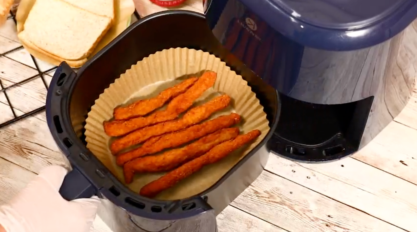 A disposable air fryer paper liner inside an air fryer with some fried food in the liner.