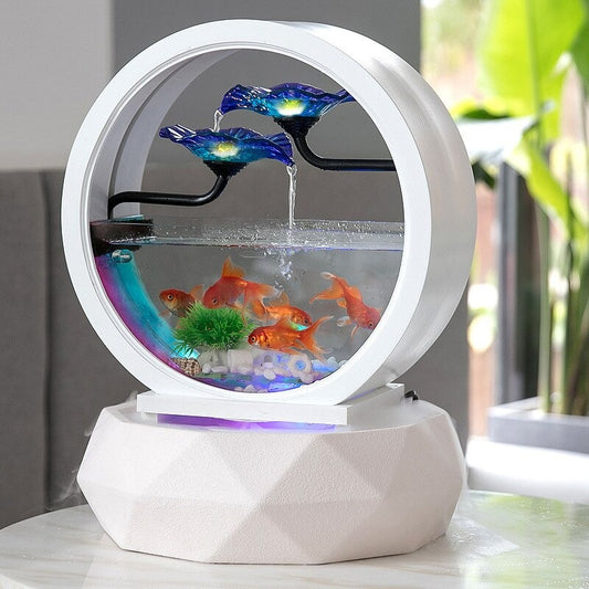 A decorative aquarium which also features a waterfall and an air purifier. There are 2 blue glass flowers on top and water is cascading down the flowers and into the aquarium where there are 5 goldfish. The base is an air purifier. The aquarium is white and circular and so is the base. There is white colored air coming out of the air purifier.