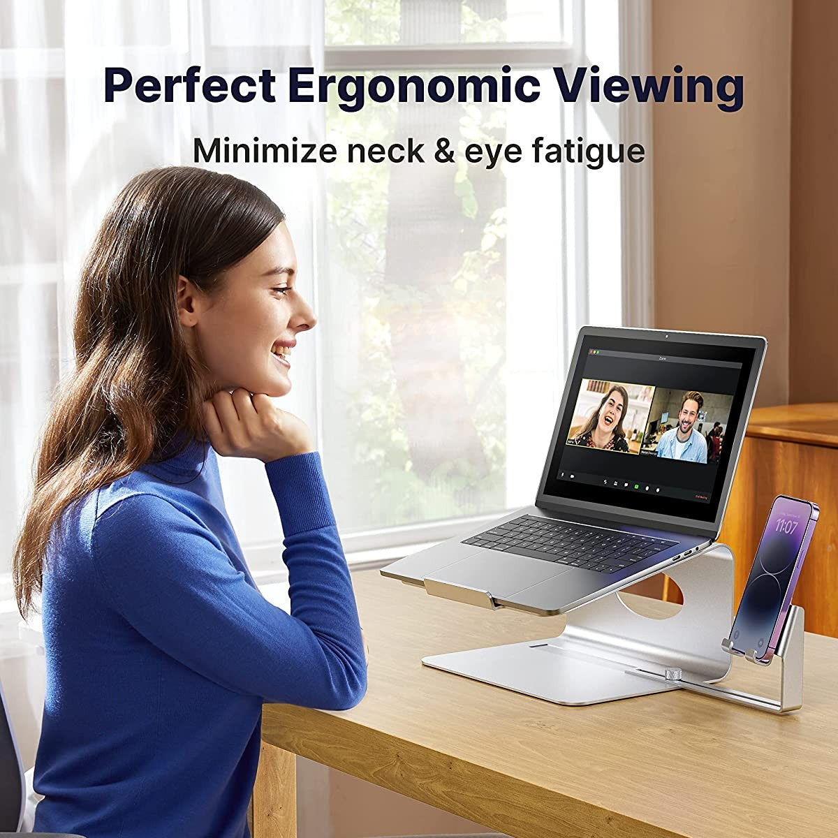 A woman is sitting in front of an open laptop using Facetime with 2 people. The laptop is on a stand. There is text which reads, 'Perfect Ergonomic viewing. Minimize neck and eye fatigue.'