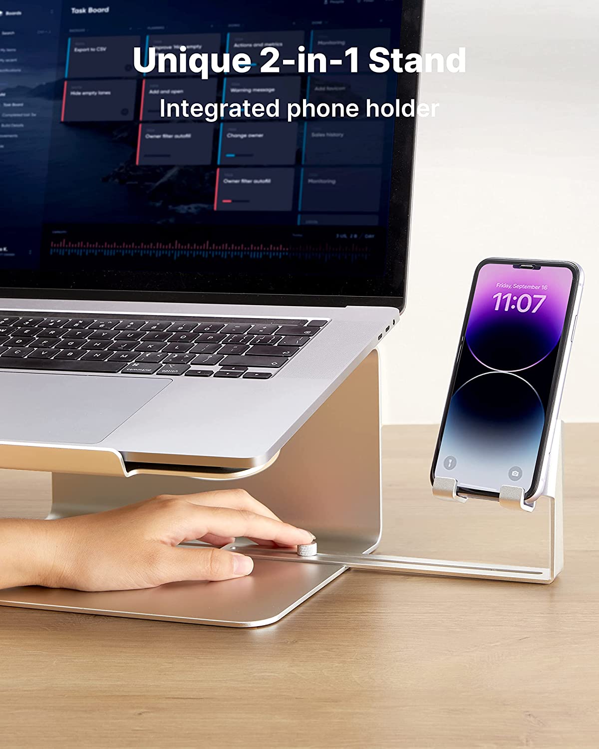 A cell phone is resting in a holder which is part of a laptop stand. The text reads, 'Unique 2-in-1 stand integrated phone holder.'
