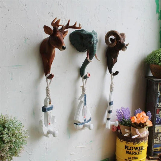Three animal shaped wall hooks on a white wall, the animals include a deer, ram and buffalo.