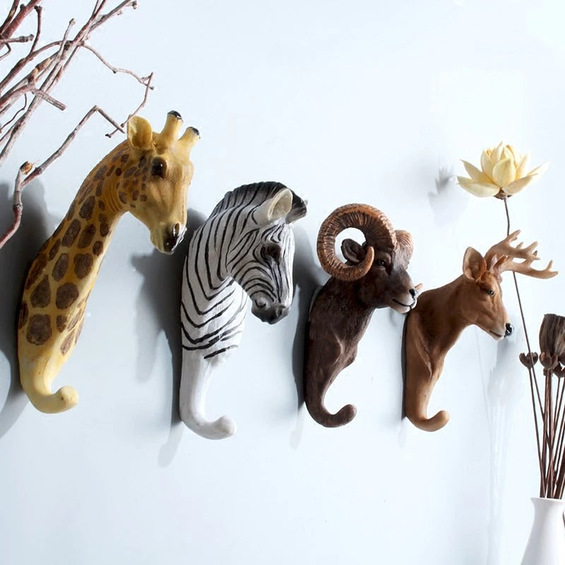 Four animal hooks on a white wall, the four animals include a giraffe, zebra, ram and deer.