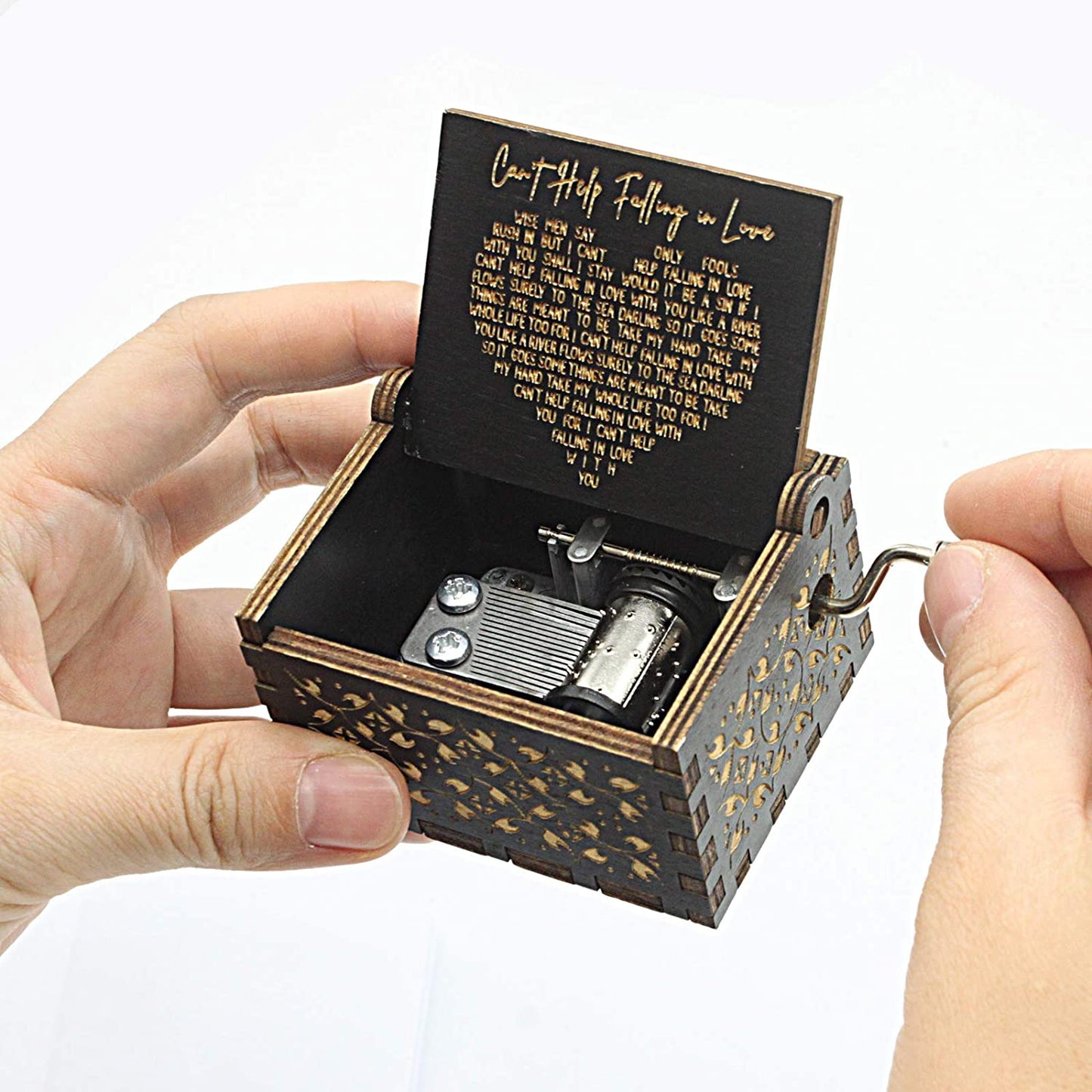 A pair of hands are holding a small wooden crank-style music box. The lyrics for the song, 'Can't Help Falling in Love' are engraved on the inside lid.