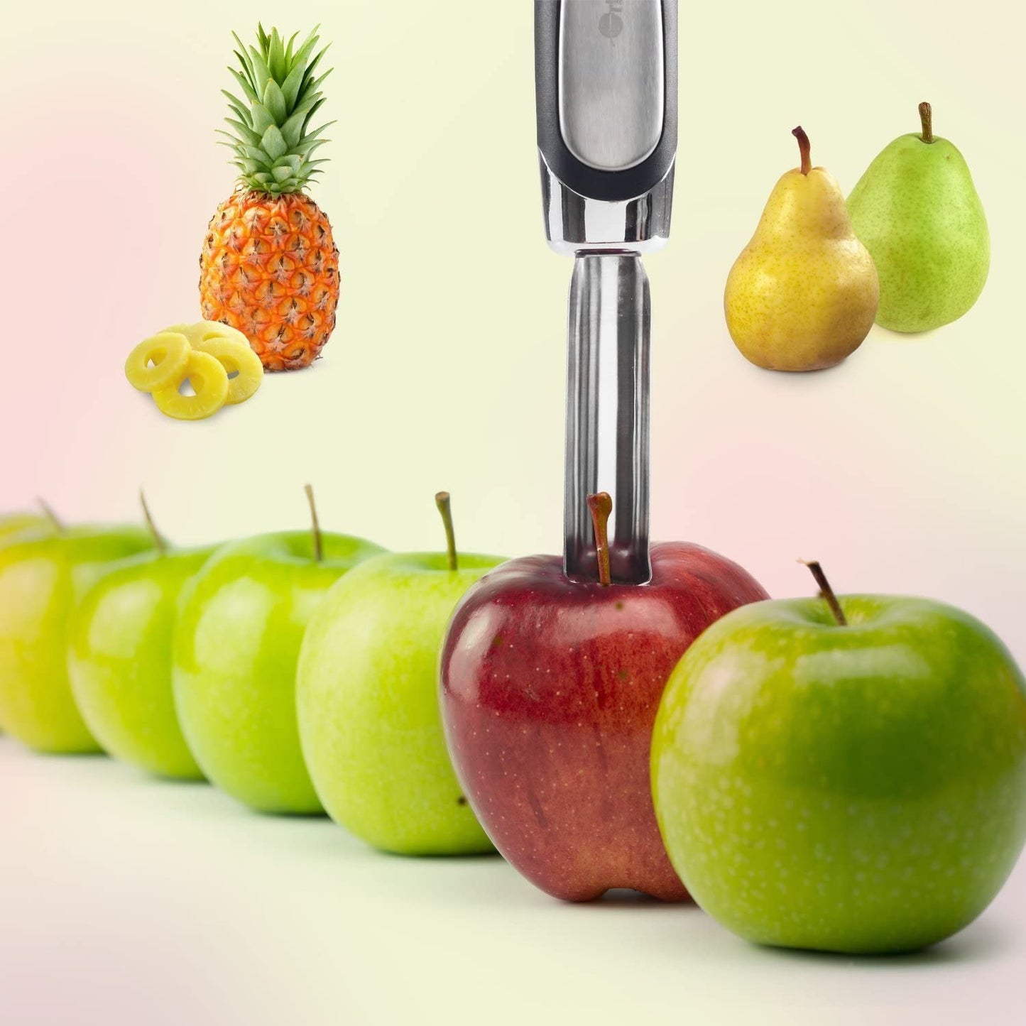 An apple corer has been placed in the centre of a red apple preparing to core out the centre. There are also green apples, two pears and a pineapple.