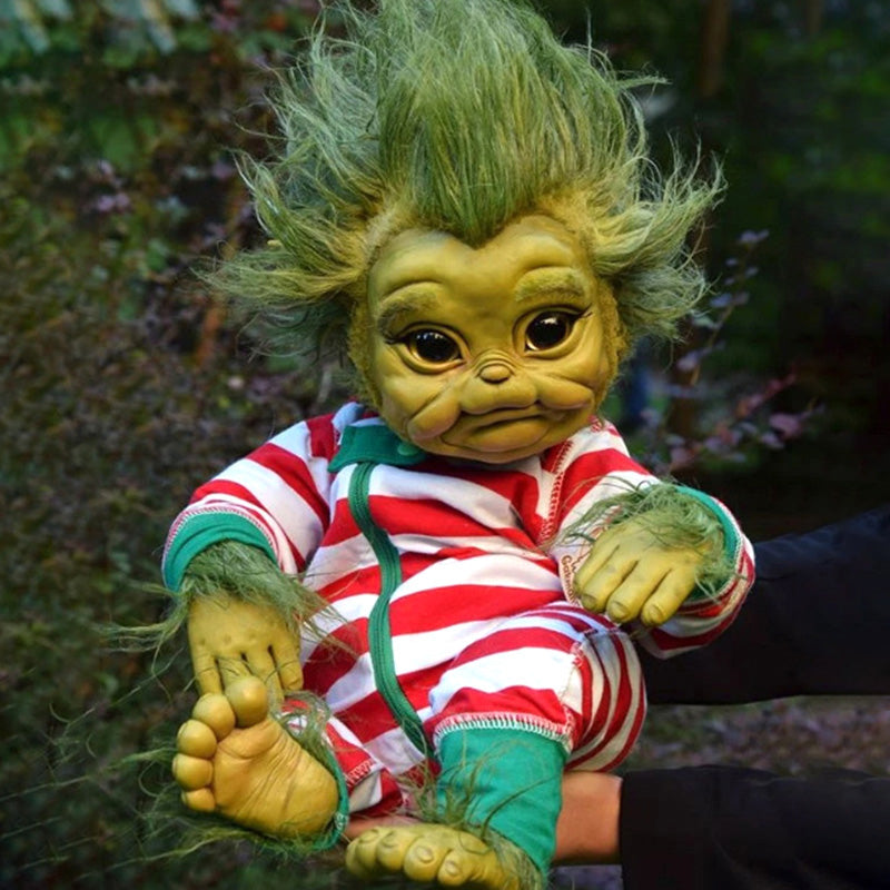 A baby grinch doll made from rubber featuring green skin and green hair wearing a red and white striped costume