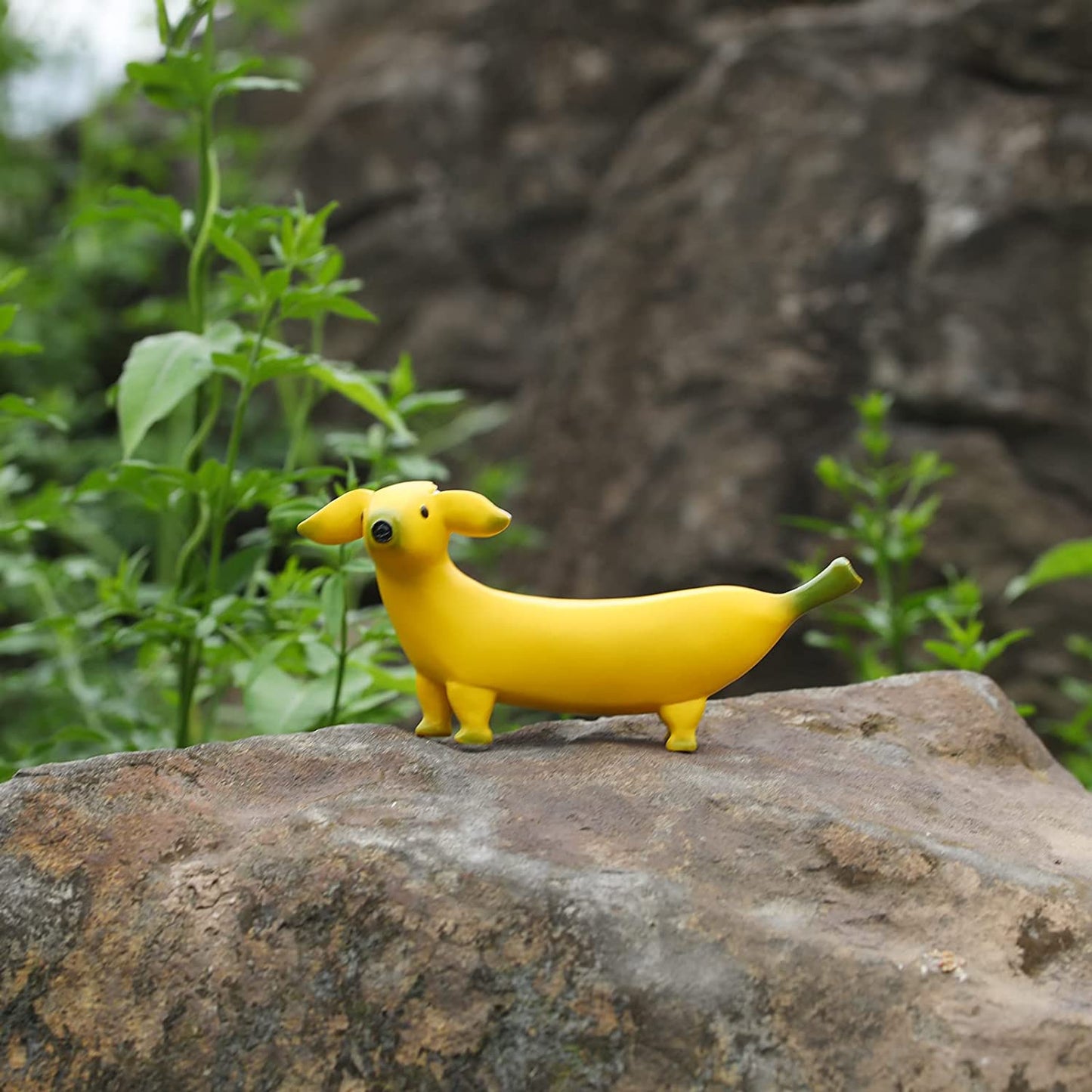 A banana dog is sitting on top of a rock. This is a garden ornament shaped like a yellow banana but with a dogs head.