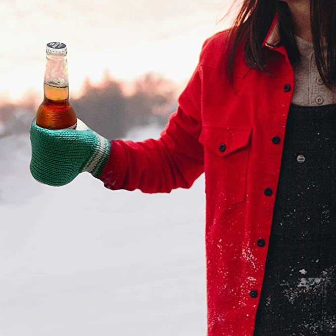 A woman in a red coat is wearing a beer mitt while holding a beer to keep her hands warm. The woman is outdoors in the snow.