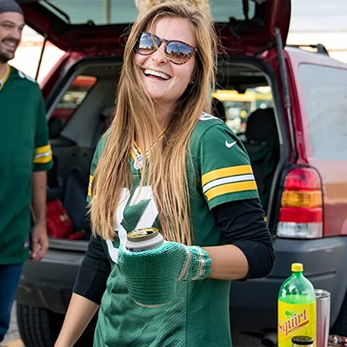 A laughing woman outdoors wearing a beer mitt which is designed to keep your hands warm while holding a cold drink.