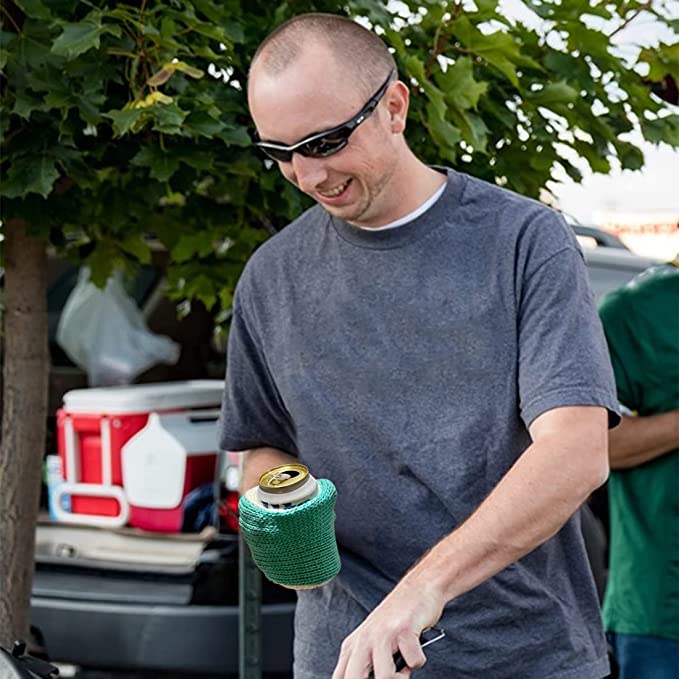 A smiling man outside wearing a green beer mitt while holding a can of beer.