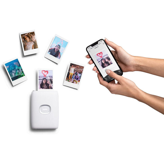 A hand is holding a cell phone next to a smartphone bluetooth printer. Various printed photos are scattered around.