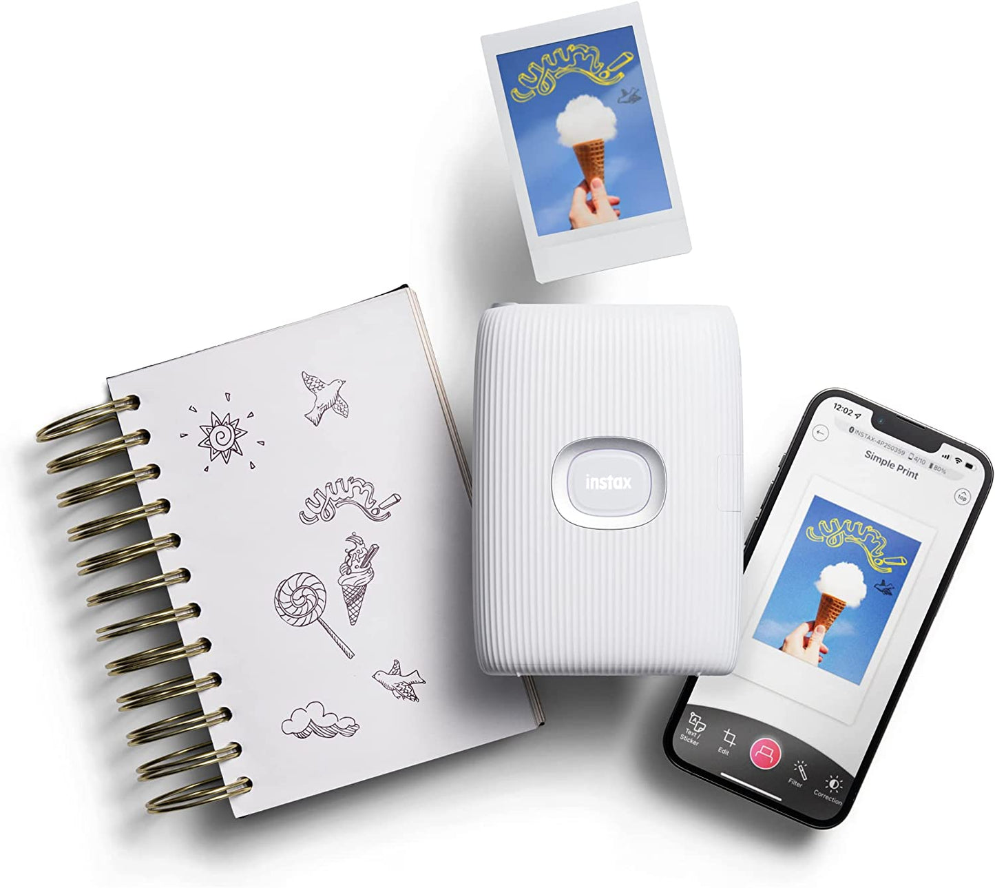 A Bluetooth smartphone printer by Instax sitting next to a smartphone. There is a printed photo of an ice cream as well as a journal with some doodles 