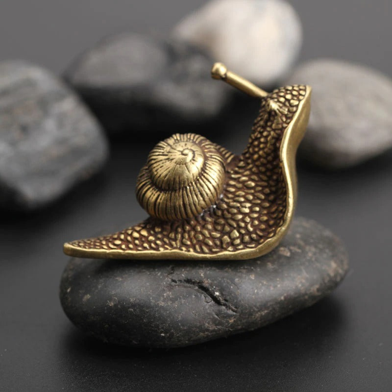 A small brass-like snail ornament sitting on a black rock.