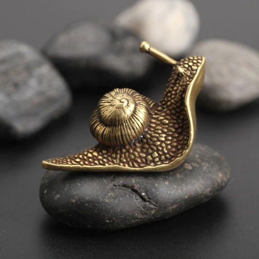 A small brass-like snail ornament sitting on a black rock.