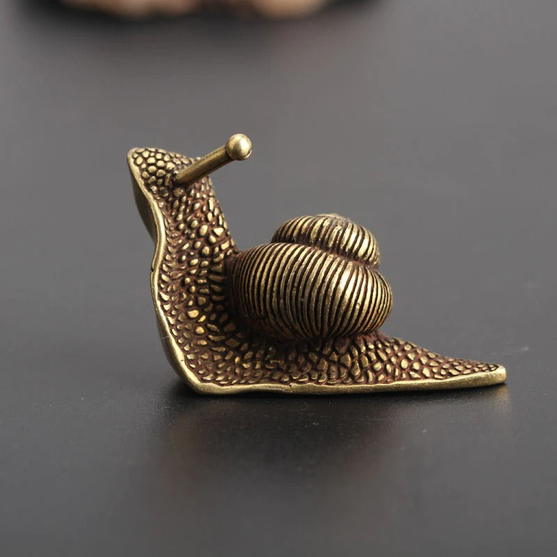 A snail home decor item which looks like it is made from brass. The snail appears to be sliding away with its head in the air.