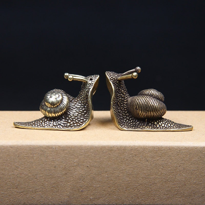 Two small snail ornaments facing each other made from pure copper but look like brass.