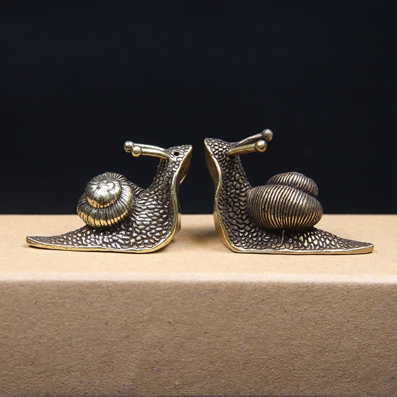 Two small snail ornaments facing each other made from pure copper but look like brass.