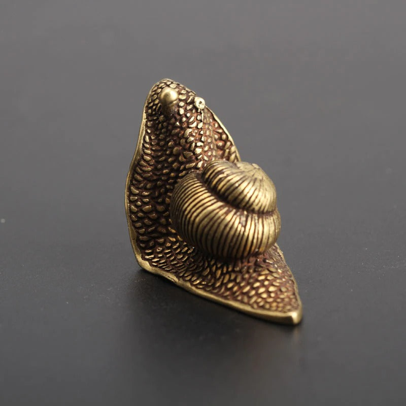 A back-view of a small snail ornament made from copper and looks like brass with a dark patina.