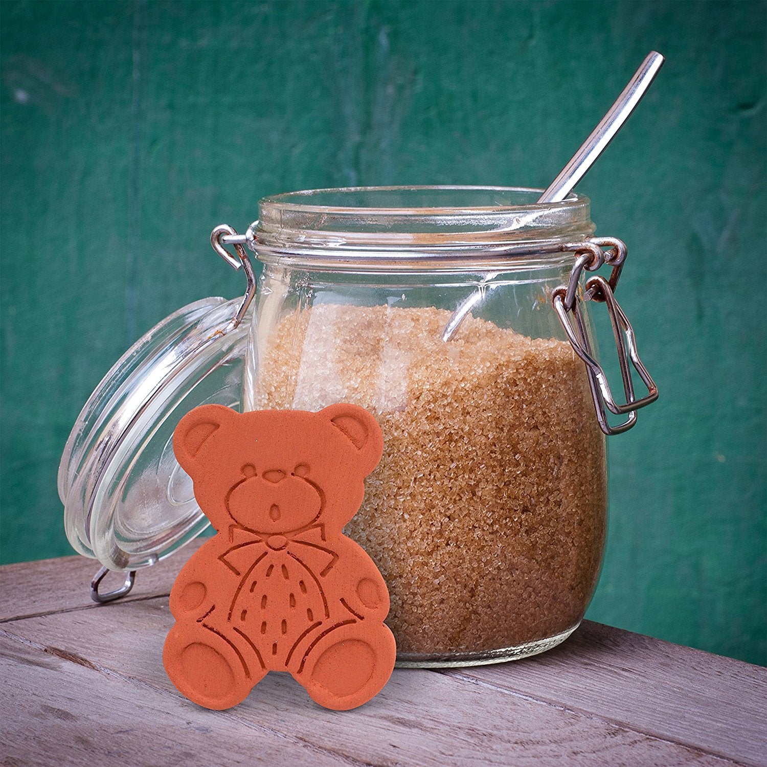 A brown sugar saver bear is sitting in front of a large jar of brown sugar.