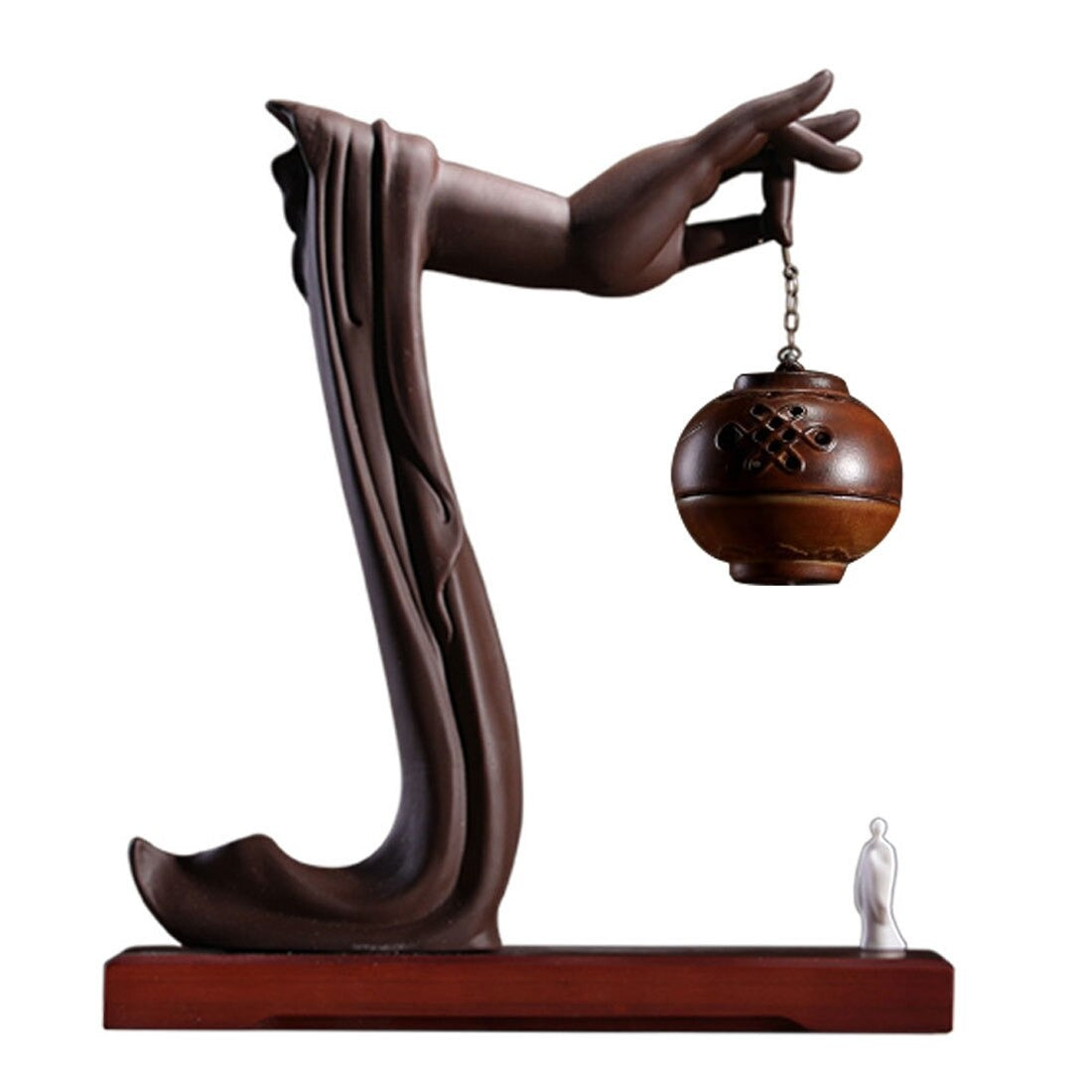 A backflow incense holder on a reddish brown base and white background. A hand is holding a red ball shaped incense burner with a white figure standing underneath,