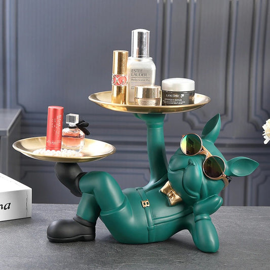 A resin bulldog serving tray. The bulldog is green and reclined in a relaxed pose holding two serving trays, one tray is held by his hand and the other is held by his foot. There are knick knacks on both trays. He is wearing a pair of cool sunglasses and a cute gold bow tie.