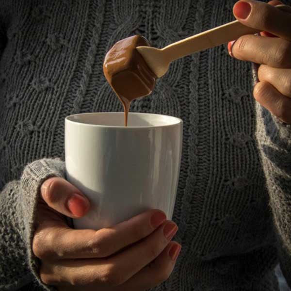 Chocolate-covered wooden spoon being stirred into a white mug of hot milk to make hot chocolate