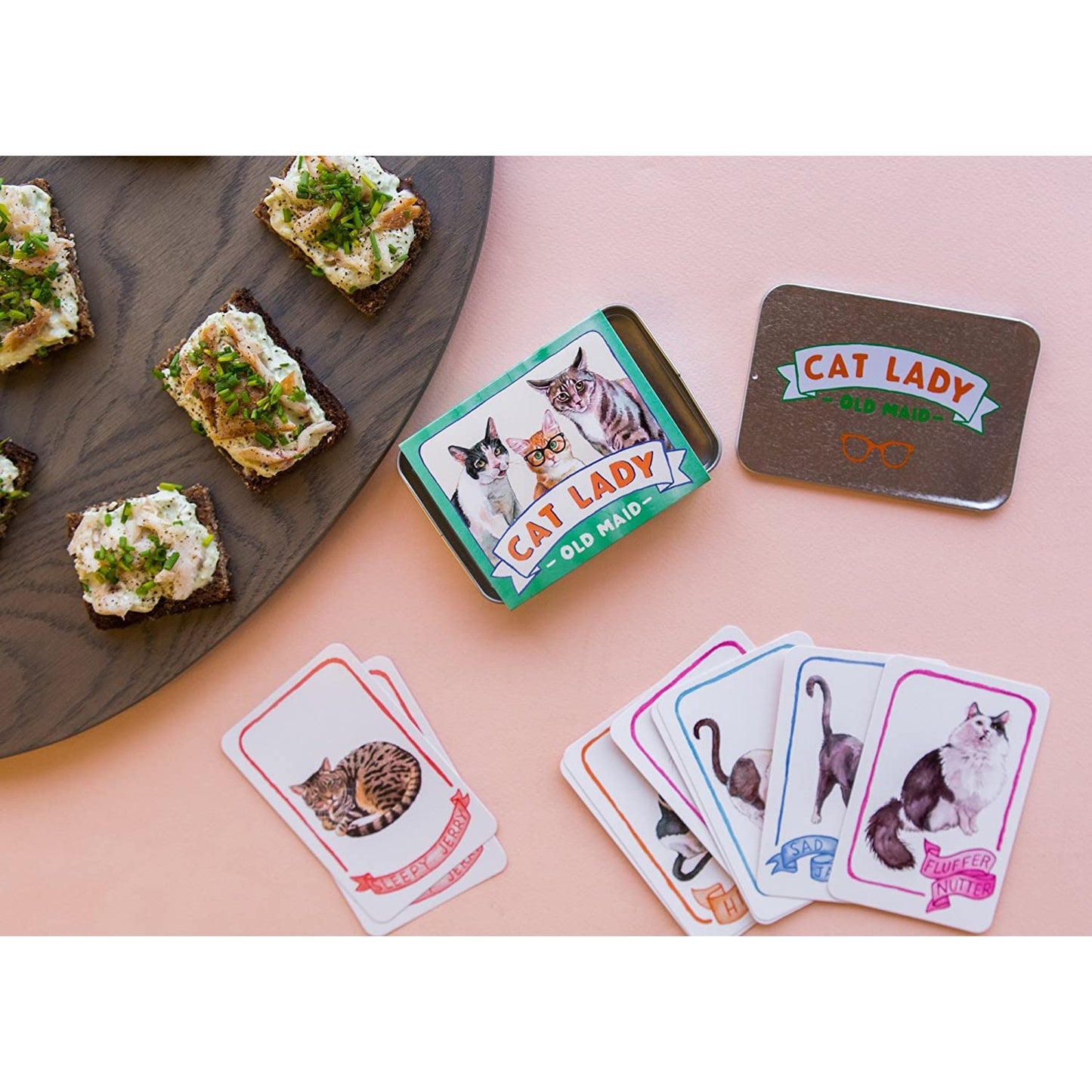 A cat lady old maid game and tin box laid out next to some food on a platter.