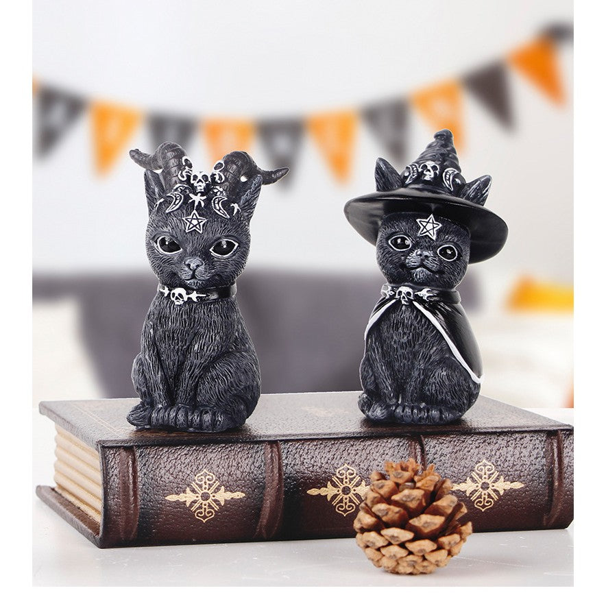 Two black cat wizard figurines standing on an old looking book.