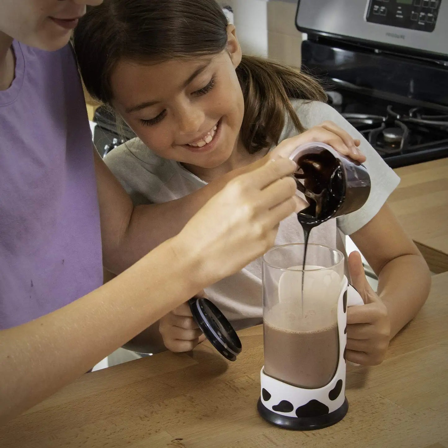 A parent and child pouring chocolate syrup into a chocolate milk automatic mixing cup