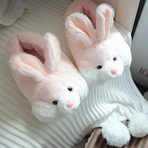 A pair of pink and white bunny slippers on a bed.