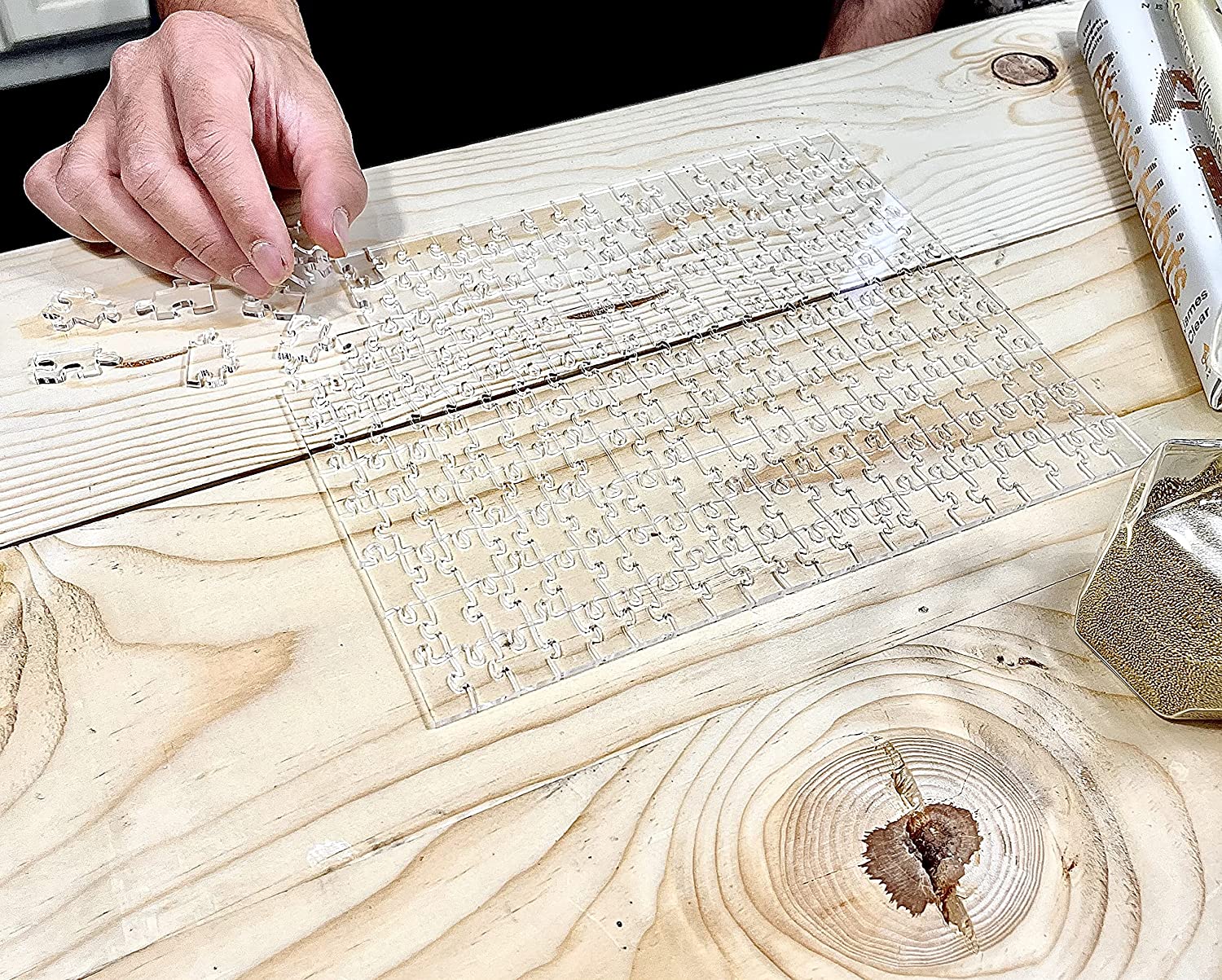 A person is sitting at a desk trying to put together a clear jigsaw puzzle on a wooden table.