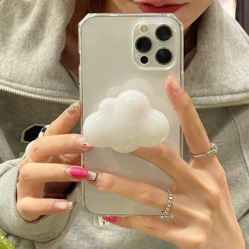 A phone grip holder in the shape of a cloud which is attached to the back of the phone case. A pair of hands is holding the phone.