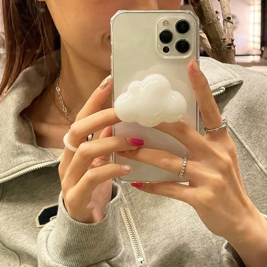 A pair of hands is holding a phone case grip holder. The holder is attached to the back of the phone and is in the shape of a cloud.