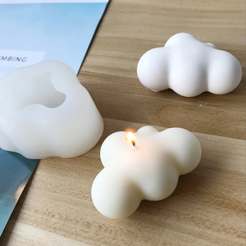 A cloud shaped silicone mold along with two cloud shaped candles which can be made using the mold.