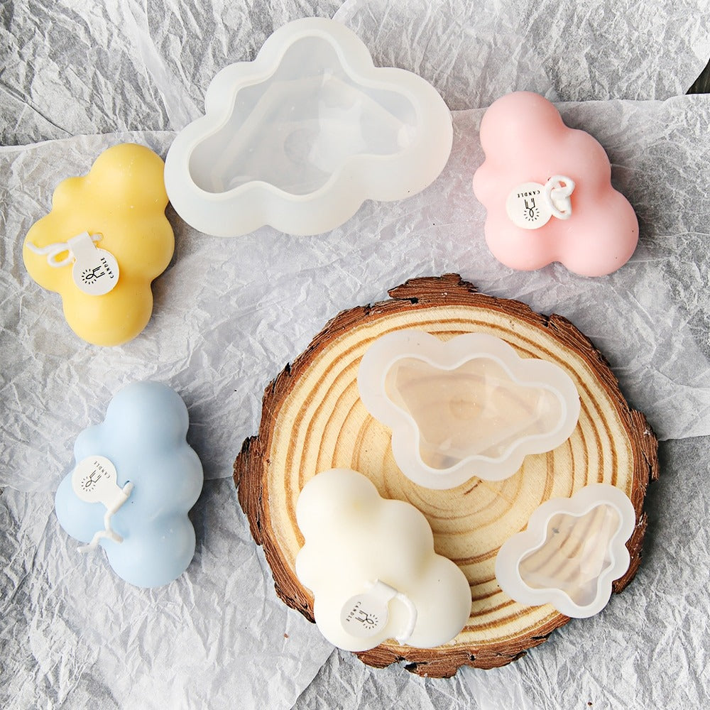 Four cloud shaped candles in pink, white, blue and yellow. There is also a 3 piece set of silicone cloud molds amongst the candles.