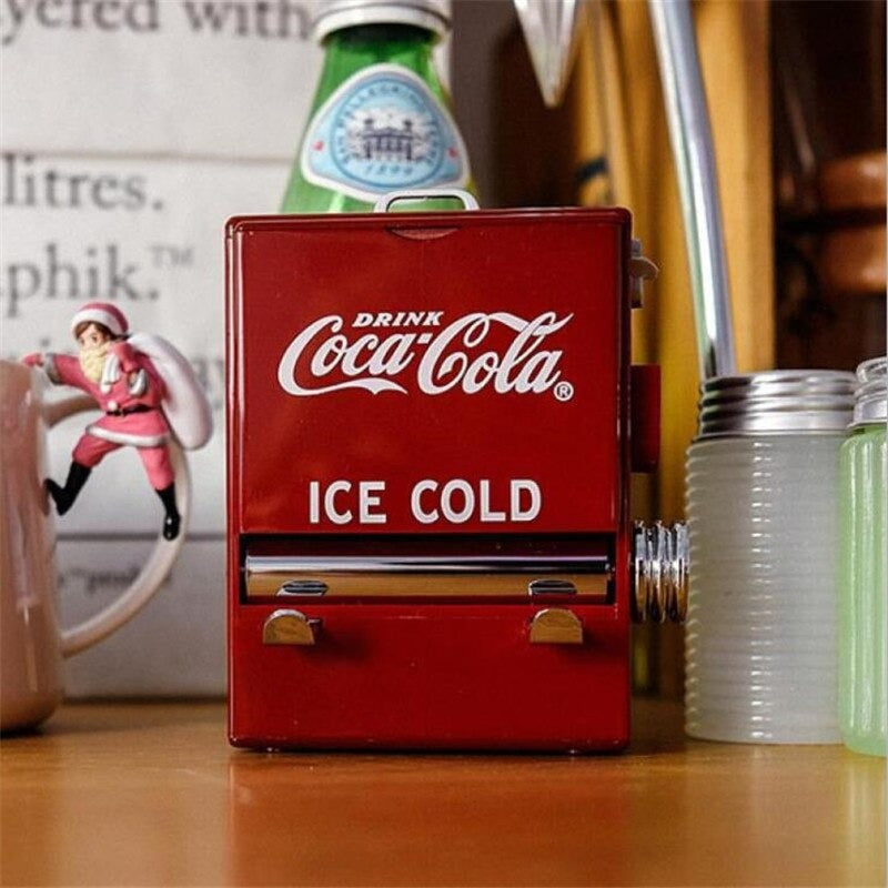 A cute red and white Coca Cola toothpick dispenser on a wooden bench.