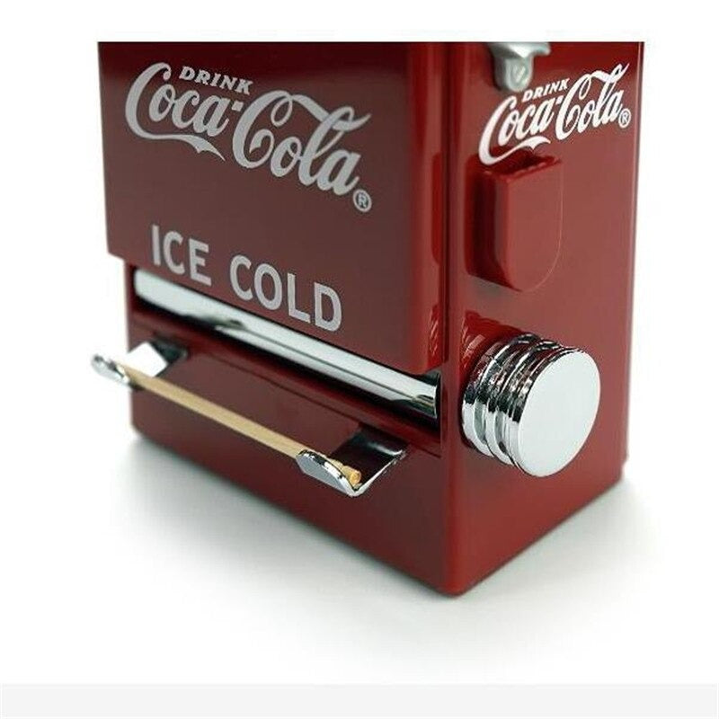 A close up view of a retro Coca Cola toothpick dispenser with a wooden toothpick dispensed out of it.
