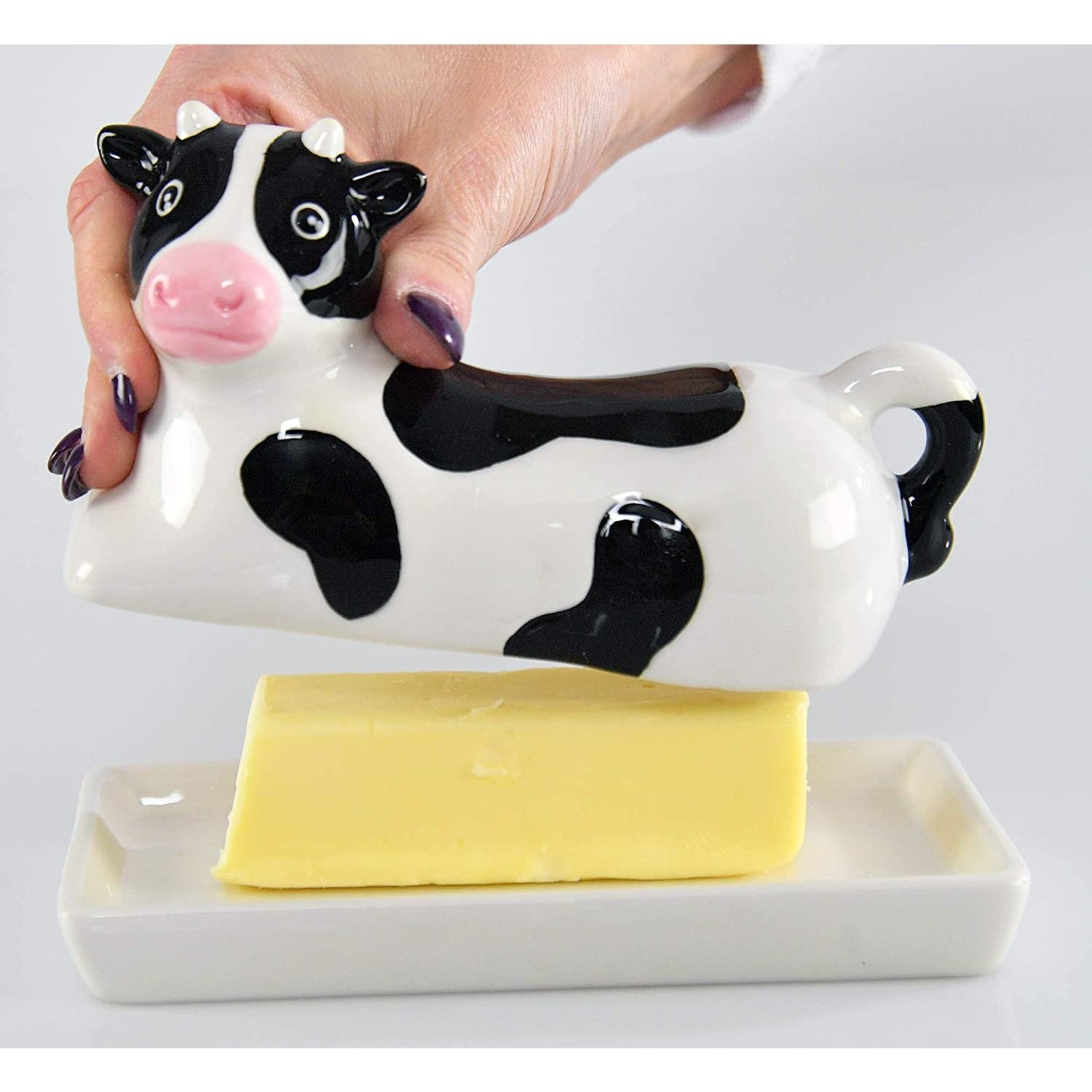 A black and white cow shaped butter dish. A hand is lifting the lid to reveal butter on the tray.