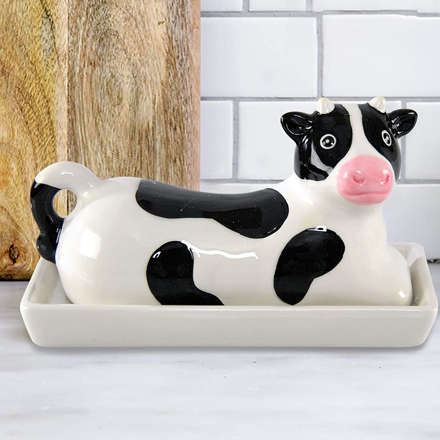 A butter dish shaped like a black and white cow is on a white bench.