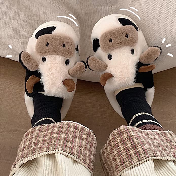 A pair of feet are wearing cow slippers. These are slippers shaped like a cow.