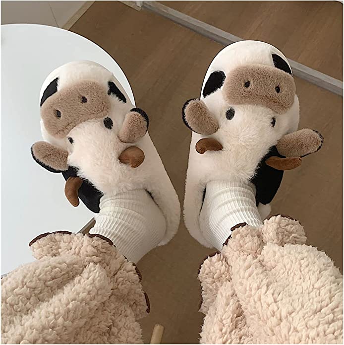 A pair of cow shaped slippers are on a pair of feet.