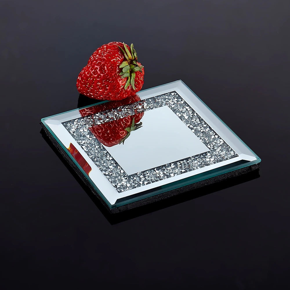 A square silver coaster which is filled with tiny crystals. There is a strawberry resting next to the coaster.
