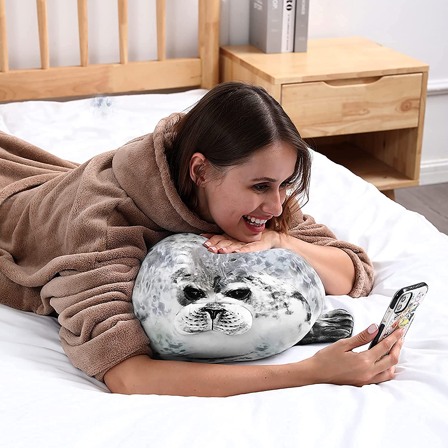 Woman laying on a bed while on the phone and cuddling with a seal pillow