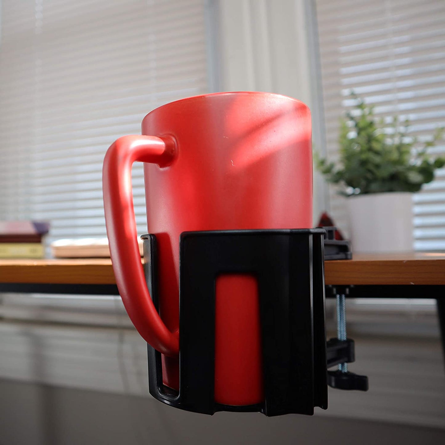 A cup holster which is attached to a desk via clamp. A red cup is securely resting in the holster.
